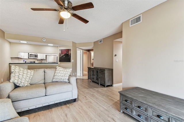 living room with ceiling fan, a textured ceiling, and light wood-type flooring