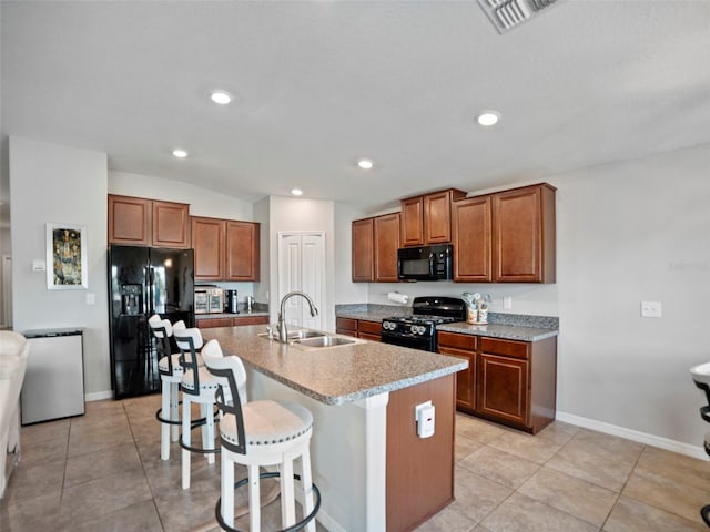 kitchen with sink, light tile patterned floors, a kitchen breakfast bar, a kitchen island with sink, and black appliances