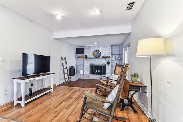 living room with a brick fireplace, wood-type flooring, and beamed ceiling