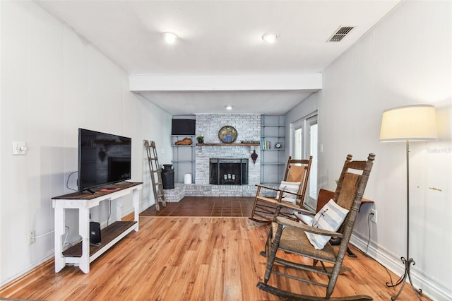 living room with built in features, wood-type flooring, and a brick fireplace