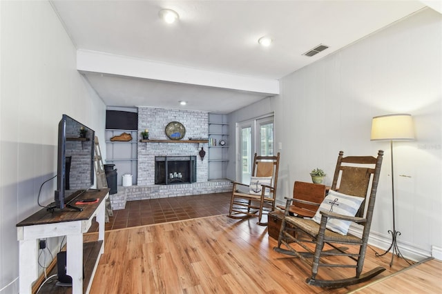 sitting room featuring beamed ceiling, hardwood / wood-style floors, a fireplace, and built in shelves