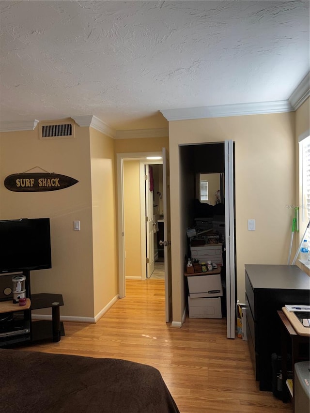 bedroom featuring ornamental molding, light hardwood / wood-style floors, and a textured ceiling