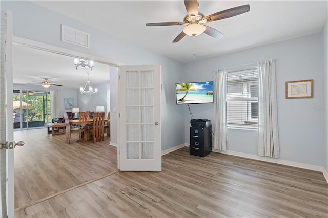 unfurnished living room with french doors, vaulted ceiling, ceiling fan with notable chandelier, and hardwood / wood-style floors