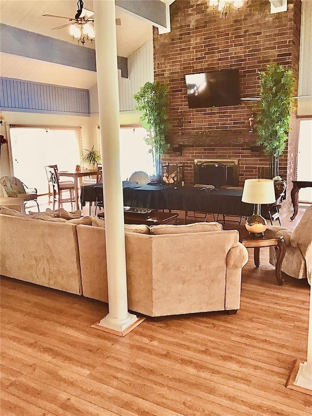 living room with a brick fireplace, decorative columns, ceiling fan, and wood finished floors