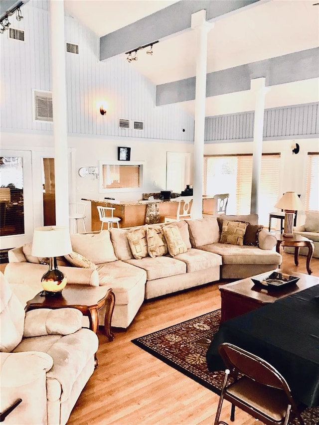 living area with a high ceiling, wood finished floors, visible vents, and track lighting