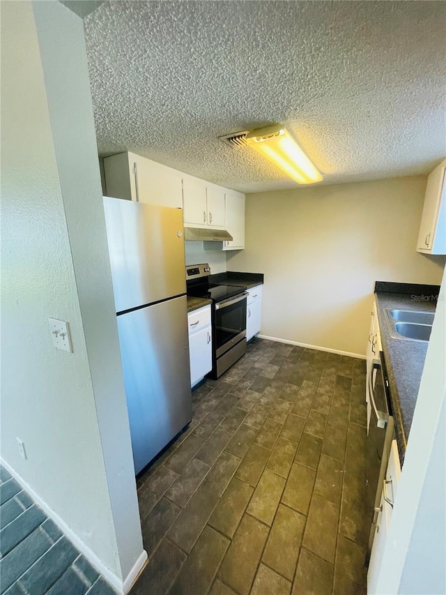 kitchen featuring baseboards, white cabinets, dark countertops, stainless steel appliances, and a sink