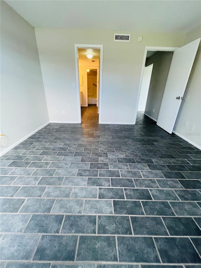 empty room with brick floor, visible vents, and baseboards