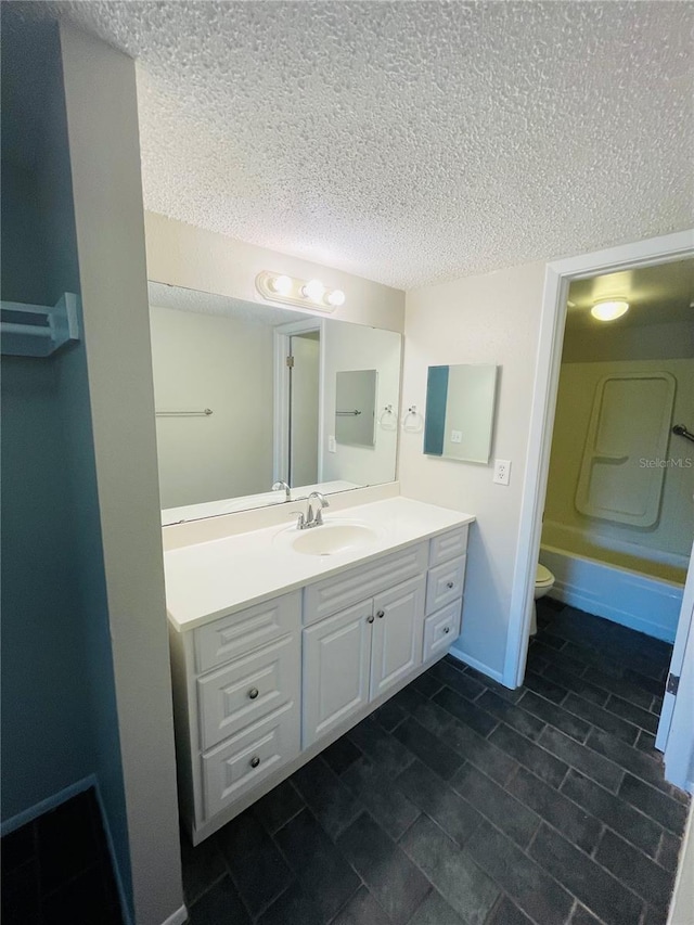 full bath with baseboards, toilet,  shower combination, a textured ceiling, and vanity