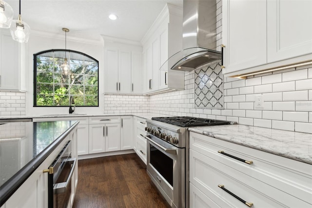 kitchen featuring wall chimney exhaust hood, stainless steel stove, pendant lighting, dark stone counters, and white cabinets