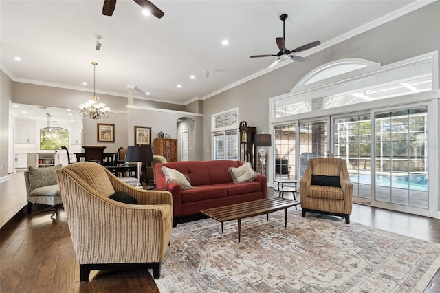 living room with hardwood / wood-style flooring, ornamental molding, a towering ceiling, and ceiling fan with notable chandelier