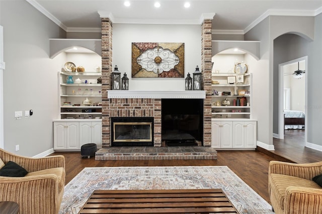 living room featuring crown molding, a brick fireplace, dark wood-type flooring, and ceiling fan