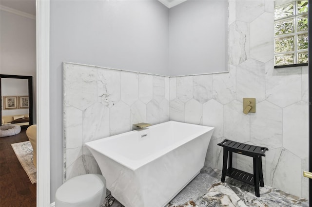 bathroom featuring tile walls, hardwood / wood-style flooring, ornamental molding, toilet, and a bath