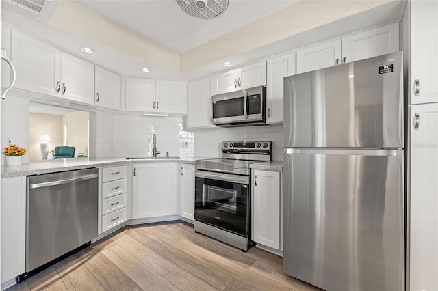 kitchen featuring sink, light hardwood / wood-style flooring, appliances with stainless steel finishes, decorative backsplash, and white cabinets