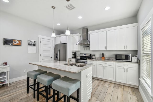 kitchen featuring wall chimney exhaust hood, sink, white cabinetry, an island with sink, and stainless steel appliances