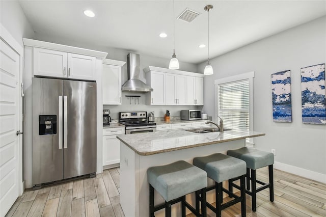 kitchen featuring wall chimney exhaust hood, appliances with stainless steel finishes, an island with sink, and white cabinets