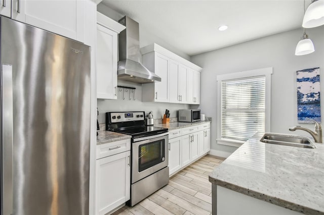 kitchen featuring white cabinets, decorative light fixtures, wall chimney exhaust hood, and appliances with stainless steel finishes