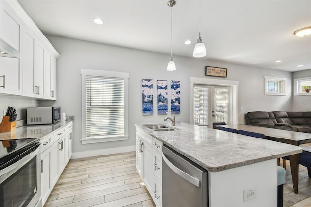 kitchen featuring sink, stainless steel appliances, an island with sink, white cabinets, and decorative light fixtures