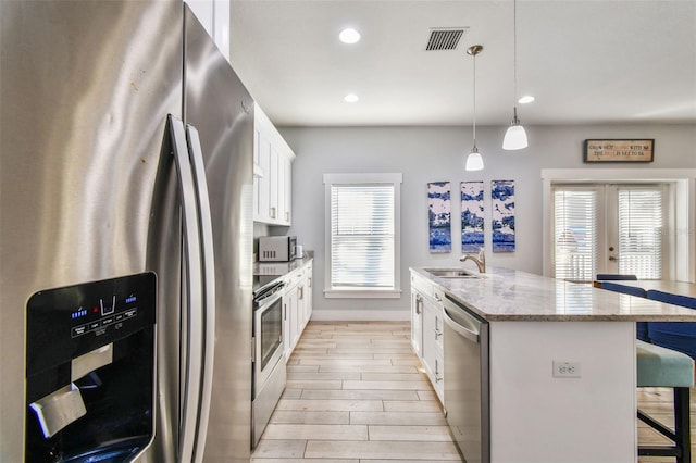 kitchen with a kitchen bar, white cabinetry, appliances with stainless steel finishes, an island with sink, and pendant lighting