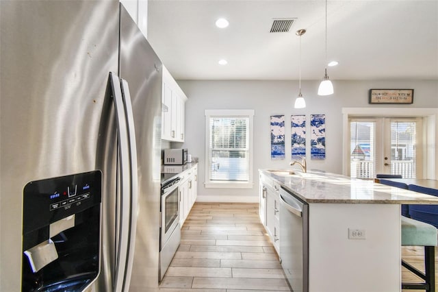 kitchen with a breakfast bar area, white cabinets, hanging light fixtures, a kitchen island with sink, and stainless steel appliances