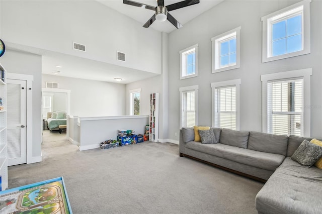 carpeted living room with ceiling fan and a high ceiling