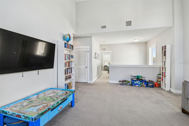 rec room with a high ceiling and light carpet