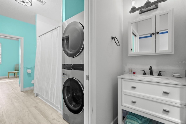 washroom featuring stacked washer / dryer, sink, and light hardwood / wood-style flooring