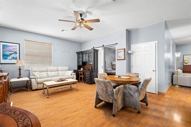 dining space featuring a textured ceiling, light hardwood / wood-style floors, a barn door, and ceiling fan