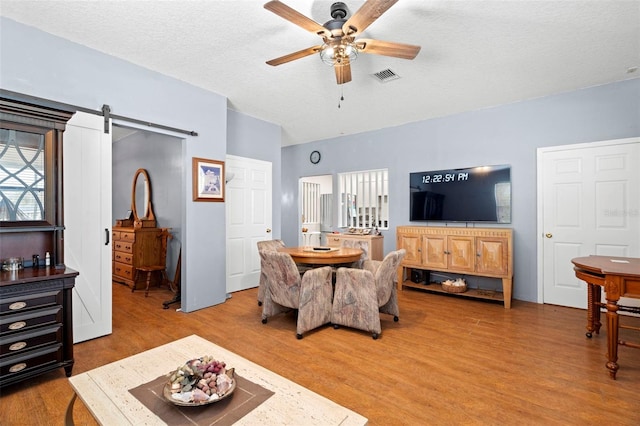 living room with a textured ceiling, wood-type flooring, a barn door, and ceiling fan