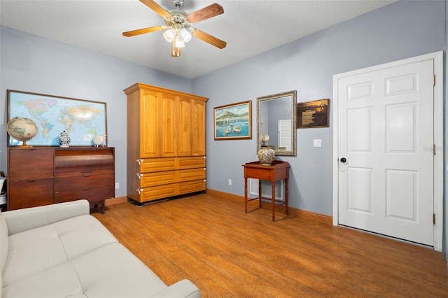 living area with hardwood / wood-style flooring, ceiling fan, and a textured ceiling