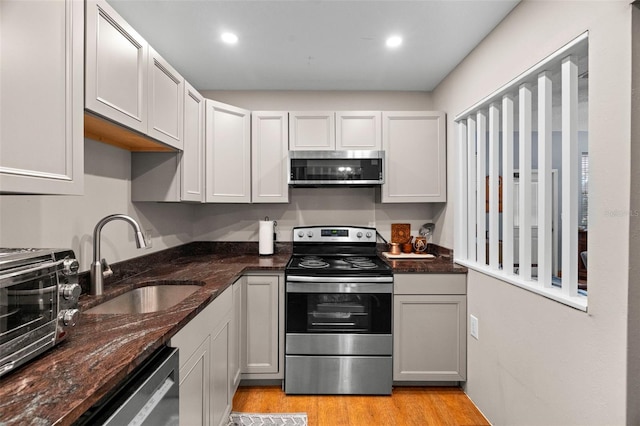 kitchen featuring dark stone countertops, sink, stainless steel appliances, and light hardwood / wood-style floors