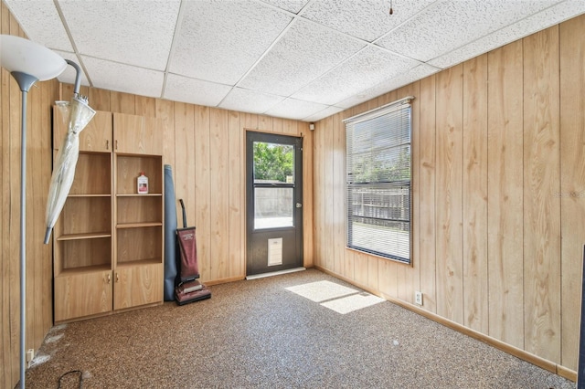 carpeted empty room with a drop ceiling and wood walls