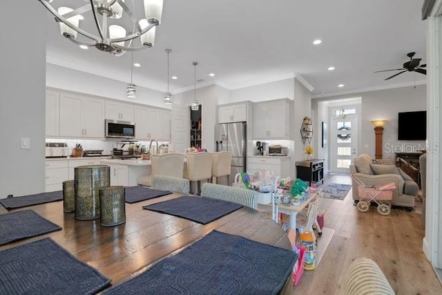 dining space featuring ceiling fan with notable chandelier, ornamental molding, and hardwood / wood-style floors