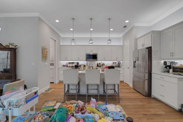 kitchen with a kitchen island, appliances with stainless steel finishes, pendant lighting, a kitchen bar, and light hardwood / wood-style flooring