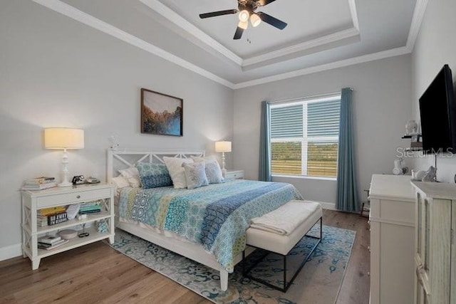 bedroom featuring wood-type flooring, ornamental molding, ceiling fan, and a tray ceiling