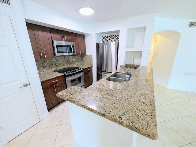 kitchen featuring light tile patterned flooring, appliances with stainless steel finishes, sink, a kitchen island with sink, and light stone counters