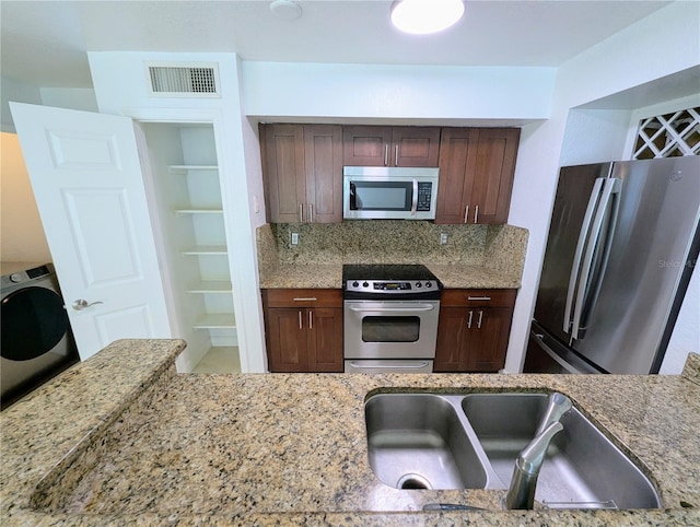 kitchen featuring washer / dryer, sink, light stone counters, stainless steel appliances, and backsplash