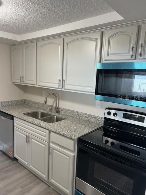 kitchen featuring sink, white cabinetry, stainless steel appliances, light hardwood / wood-style floors, and a textured ceiling