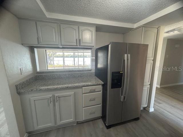 kitchen featuring hardwood / wood-style flooring, light stone countertops, stainless steel fridge with ice dispenser, and a textured ceiling