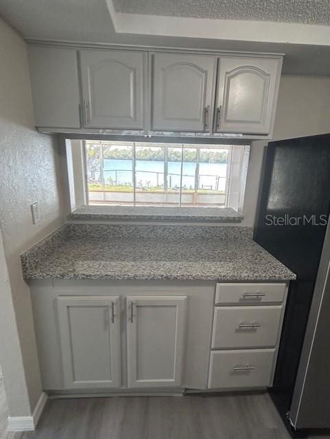 kitchen with hardwood / wood-style flooring, light stone counters, and white cabinets