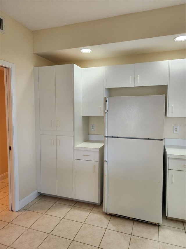 kitchen with white refrigerator, light tile patterned floors, and white cabinets