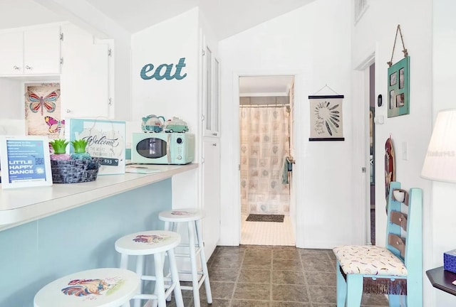 kitchen featuring dark tile patterned floors, vaulted ceiling, and white cabinets