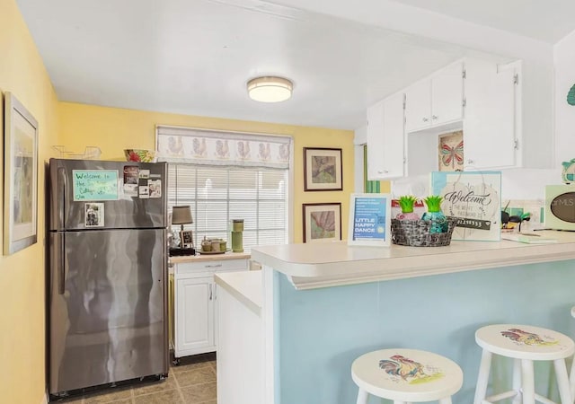 kitchen featuring stainless steel fridge, a breakfast bar area, kitchen peninsula, and white cabinets