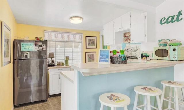 kitchen featuring stainless steel refrigerator, white cabinetry, a kitchen breakfast bar, and kitchen peninsula