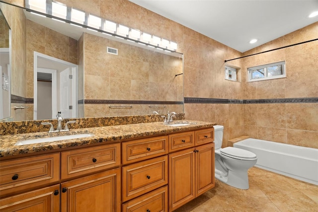 full bathroom featuring tile patterned floors, toilet, tiled shower / bath, tile walls, and vanity