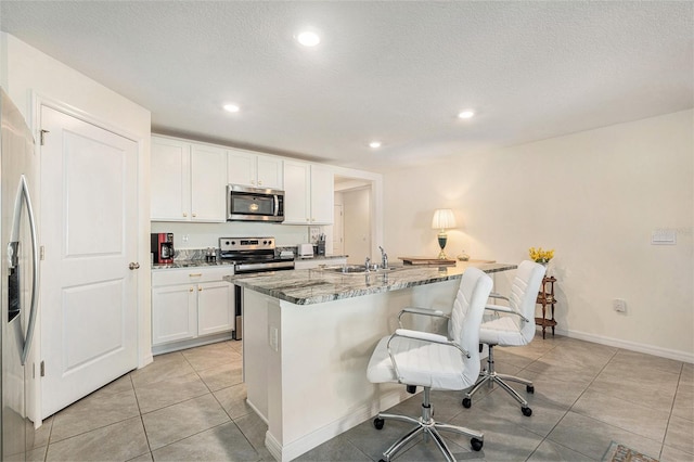 kitchen with sink, white cabinetry, dark stone countertops, an island with sink, and stainless steel appliances