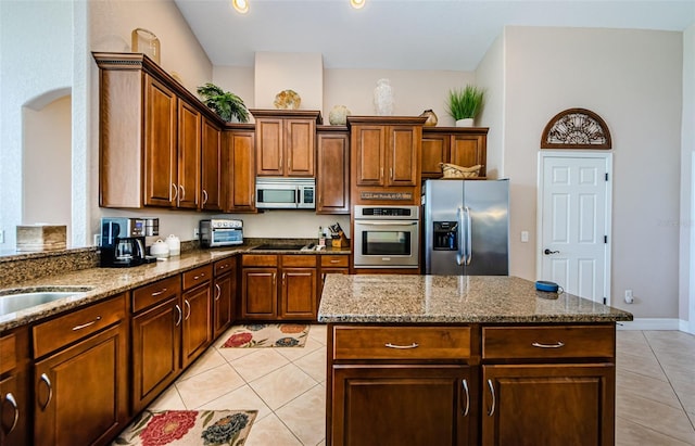 kitchen with a kitchen island, appliances with stainless steel finishes, stone countertops, sink, and light tile patterned floors