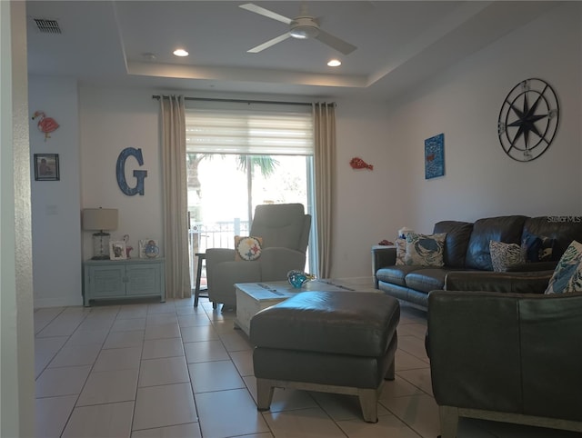 living room featuring a raised ceiling, ceiling fan, and light tile patterned flooring