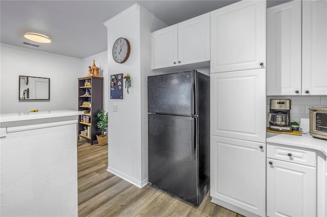 4221 W Spruce St Unit 1325, Tampa, FL 33607 - kitchen with black refrigerator, white cabinetry, tasteful backsplash, and light wood-type flooring