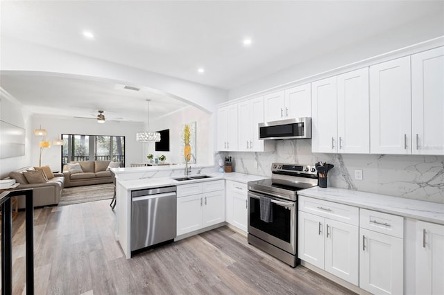 kitchen with appliances with stainless steel finishes, kitchen peninsula, sink, and white cabinets