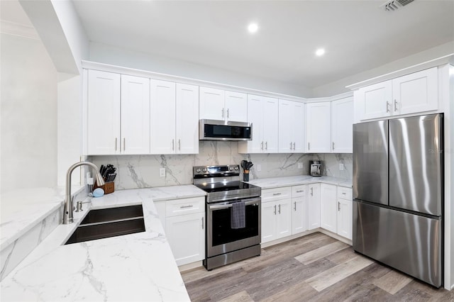 kitchen with stainless steel appliances, sink, white cabinets, and light stone counters